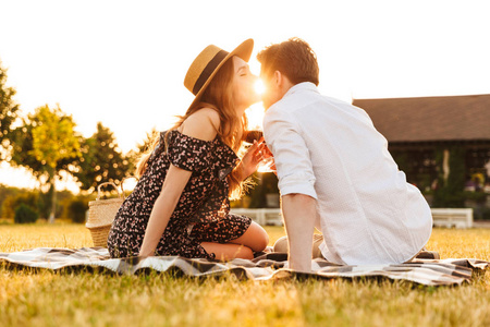 年轻可爱情侣的形象坐在一起约会 outdors 在野餐举行葡萄酒接吻酒杯