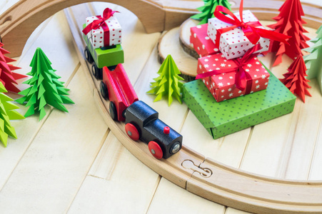 一辆玩具木制火车运载一个箱子与礼物对孩子。圣诞魔术城纸树和星星, 装饰为节日。新年玩具