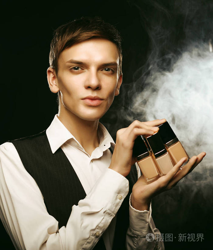 美的概念.年轻的男性化妆师在黑暗的背景下装扮成粉底
