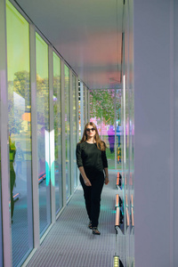 一个女孩的肖像站在一个阳光明媚的一天公园玻璃墙之间的走廊上