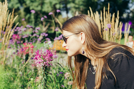 在一个温暖的阳光明媚的日子, 一个女人的肖像在城市公园里闻到一朵花的香味。