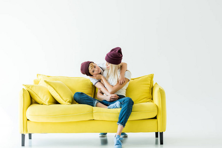 母亲和儿子在勃艮第帽子拥抱白色的黄色沙发上