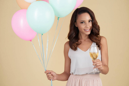 微笑美丽的女人与波浪的发型持有一堆彩色氦气球和香槟玻璃