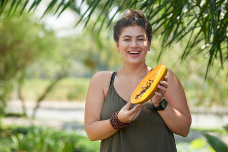 快乐的年轻女子手持成熟的木瓜在手, 阳光明媚的绿色公园背景