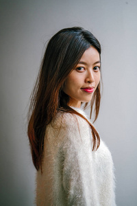 时尚和时尚的年轻的中国亚洲妇女摆姿势。她穿着一件漂亮的白色毛衣。