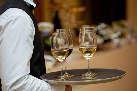托盘上有白葡萄酒的眼镜。和客人见面。侍者带着一盘酒。