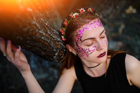 一个年轻漂亮的女人, 她的脸上有紫罗兰色的光芒, 站在一棵被烧毁的树旁