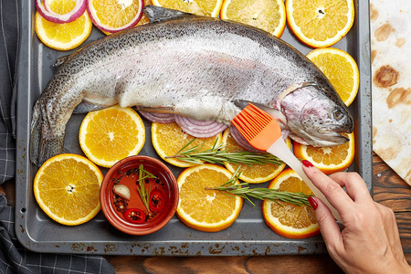 新鲜鲑鱼躺在烤盘上的橙子。手厨师用刷子涂片鲑鱼油。烹调鲑鱼的概念