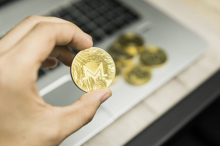 男性商人手中持有 Monero 硬币的背景下笔记本电脑键盘和成堆的金币。虚拟货币和金融增长概念。Moneros 贸易开采