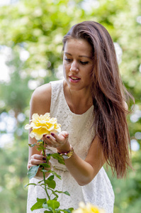 年轻女孩在一个白色礼服在夏天公园嗅到玫瑰