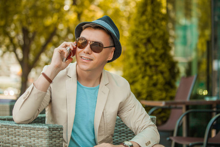一个戴着帽子和墨镜的男人在电话旁微笑着公园旅行和生活方式的概念