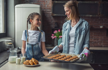 妈妈和女儿正在看着对方, 微笑着, 而妈妈正在家里厨房里拿着新鲜出炉的饼干。