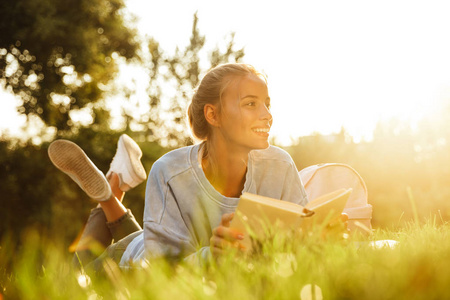 一个快乐的年轻女孩的肖像躺在草地上的公园, 阅读一本书
