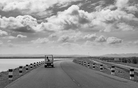 景观黑白相间的风景公路上的空公路和电动高尔夫球车附近的一个大水库与天空和云背景。Sak Jolasid 大坝泰国
