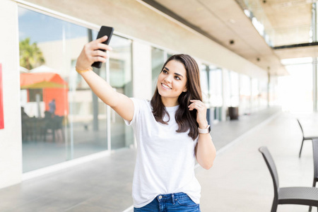 微笑的中年女性博客自拍使用智能手机在购物中心