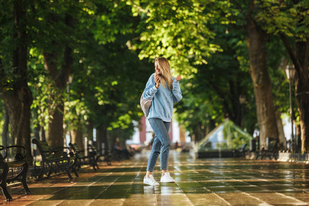 快乐的女孩与背包手持手机, 在公园散步