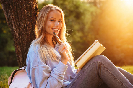 一个快乐的年轻女孩的肖像坐在草地上的公园, 读一本书, 做笔记