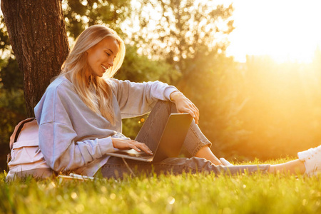 一个可爱的年轻女孩的肖像坐在草地上在公园的草坪上, 使用笔记本电脑