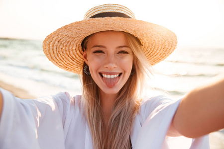 时尚快乐的女人的照片20s 在夏天稻草帽子笑, 并采取自拍, 而在海滩上散步
