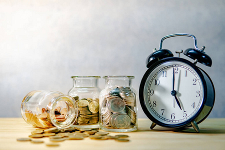 时钟与硬币在货币玻璃罐子和溢出在木桌上。为未来的退休存钱。金融业务增长。时间投资理念