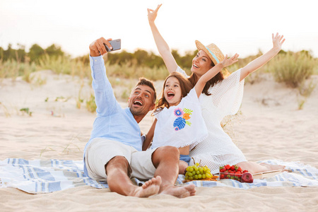 年轻可爱快乐的家庭的形象在海滩上一起玩的开心在户外做自拍手机