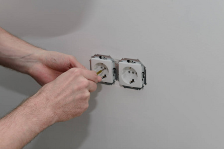 电工的手是用螺丝刀在墙上安装白色插座。