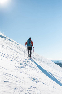 一个人爬上山顶。登山运动员在雪地鞋背着一个背包。在冬天的山上旅行。大自然中的极端假期。极端条件下的旅游者