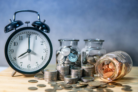时钟与硬币在货币玻璃罐子和溢出在木桌上。为未来的退休存钱。金融业务增长。时间投资理念