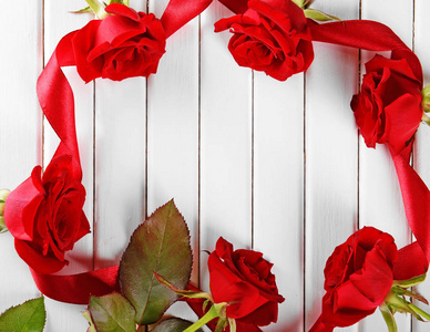 白色木质背景上美丽的红玫瑰和丝带制成的框架