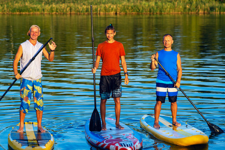 快乐的朋友们, 在日落时冲浪者在大河上放松, 享受生活。站起来桨登机可怕的主动户外娱乐