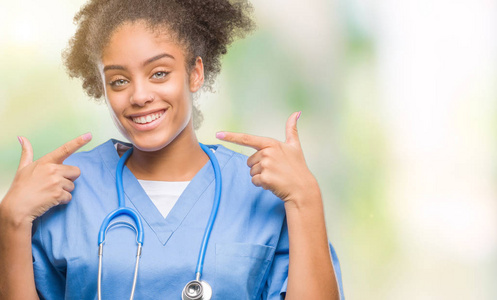 年轻的美国黑人医生在孤立的背景下微笑着自信地显示和指着手指的牙齿和嘴巴。健康理念