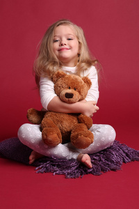 穿睡衣的女孩拥抱熊，坐在披肩上。 红背