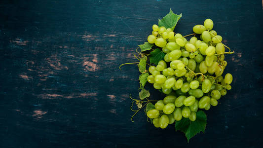 新鲜的绿色葡萄与叶子的葡萄。顶部视图。在黑色的木质背景。文本的可用空间