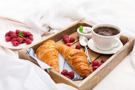 床上有杯咖啡和羊角面包早餐
