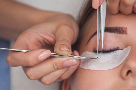 化妆大师纠正，并加强睫毛梁伸出一把镊子在一家美容院。专业护理对皮肤和眼睛
