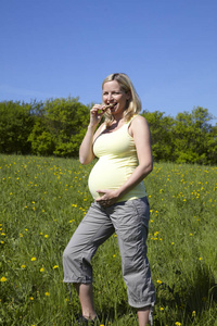 愉快的孕妇在夏天衣服吃麦片粥在草地上阳光明媚的一天