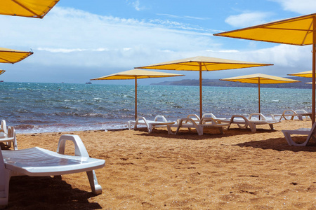 在阳光明媚的日子, 沙滩上的躺椅和五颜六色的雨伞, 黄色的沙子和蓝色的水