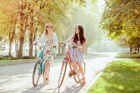 两个年轻女孩与在公园里骑自行车