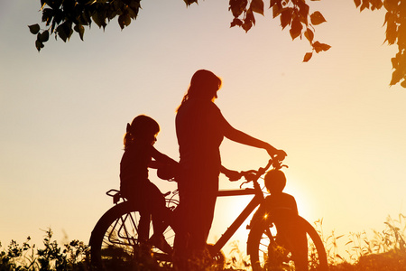 母亲带着儿子和女儿骑自行车在日落时