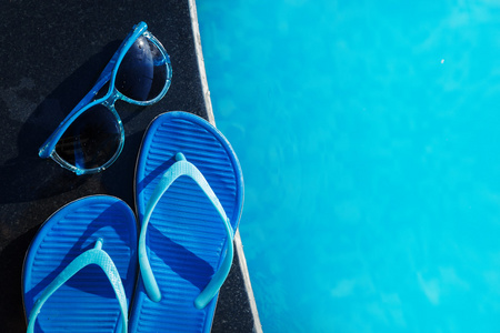 蓝色拖鞋和太阳镜上边框的游泳池