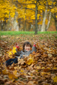 小女孩向树叶扔在秋天的公园