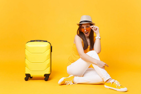 旅行者在夏季休闲服装, 帽子坐在黄色橙色背景的手提箱。在周末外出旅行的女乘客。航空旅行概念