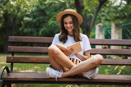 快乐的女孩读一本书, 而坐在公园户外