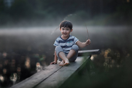 坐在湖边木码头上的微笑男孩