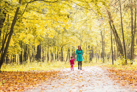 母亲和女儿在公园散步手牵着手。家庭生活方式，深秋季节概念