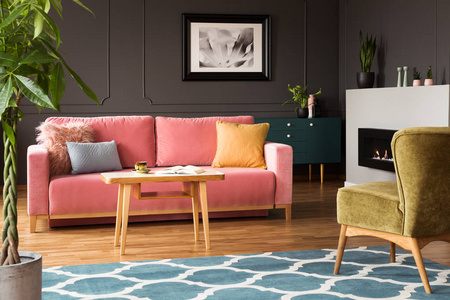 绿色扶手椅和粉红色沙发在五颜六色的客厅内部与蓝色地毯和海报。真实照片