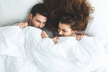 在床上躺在白色毯子下的快乐年轻夫妇的最高视图
