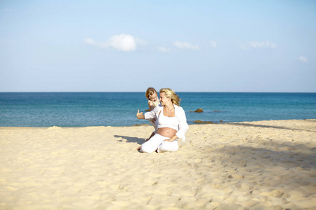 年轻孕妇坐在沙滩上与女儿玩耍