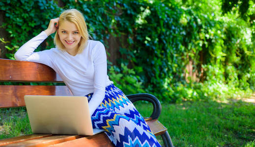利用免费无线网络的优势。女自由职业者在公园工作。妇女与笔记本电脑工作室外, 绿色自然背景。女孩坐在长椅上用笔记本。wifi 网