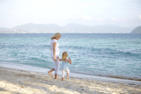 年轻孕妇与女儿在海边散步